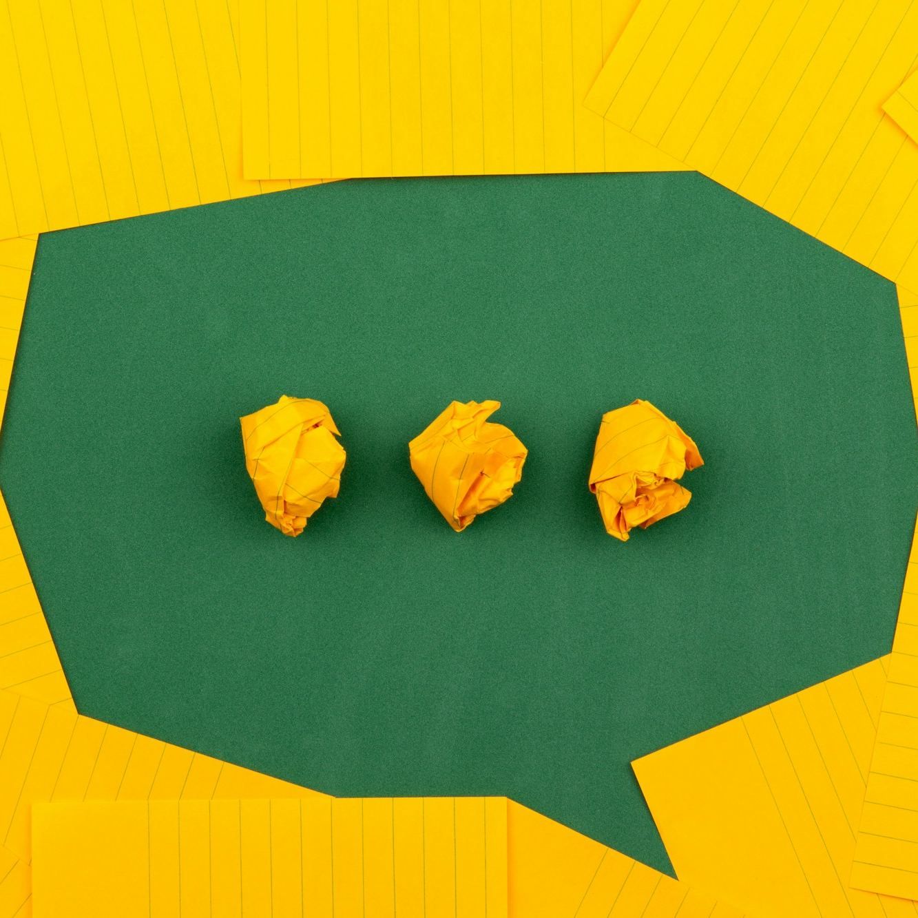 A green paper speech bubble with three crumpled-paper dots, on a honey-yellow background of lined pages