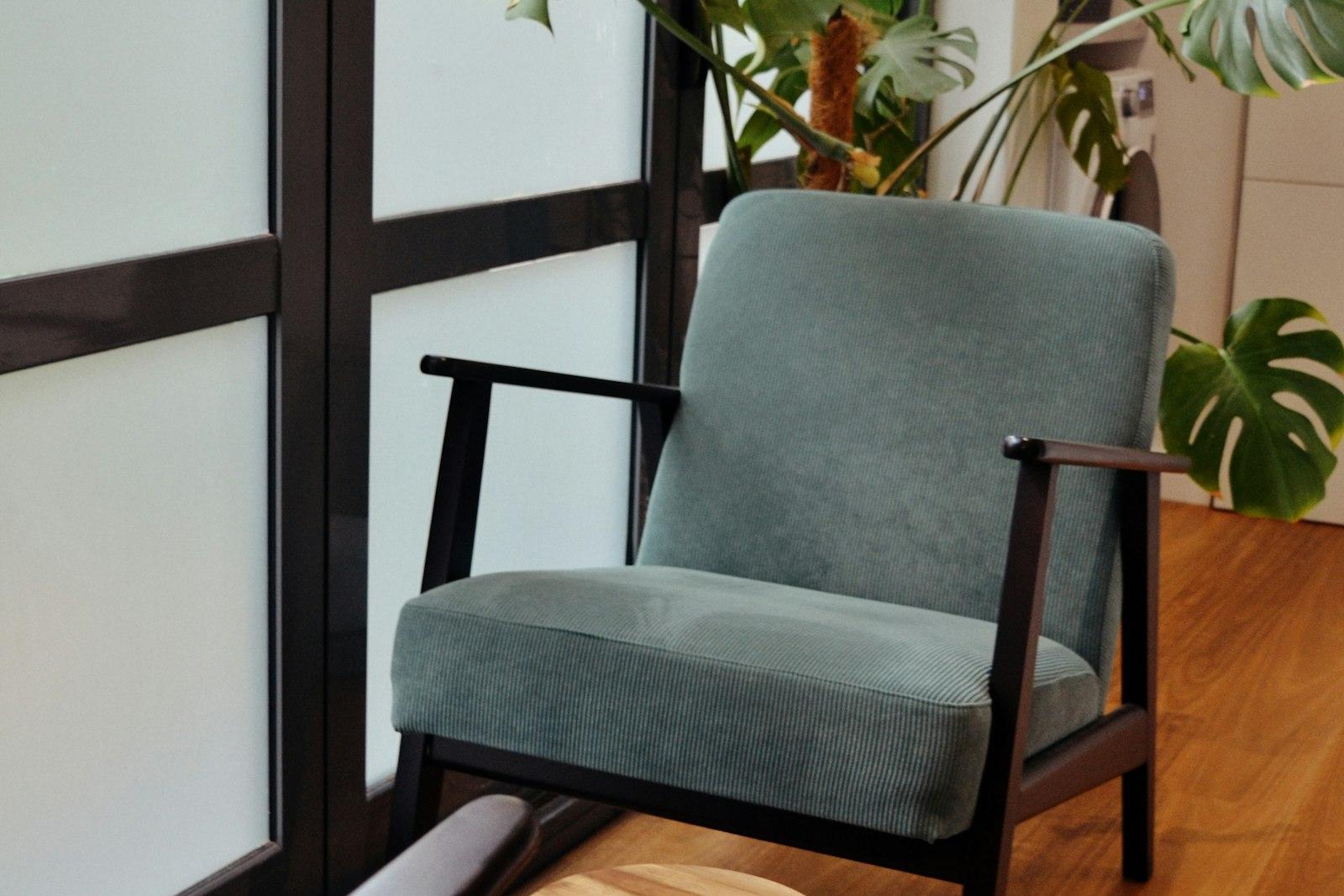 A softly upholstered armchair beside a bright window in a calm, plant-filled treatment room